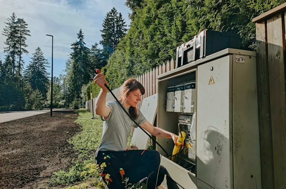 Female electrician pulls cables from green electrical box