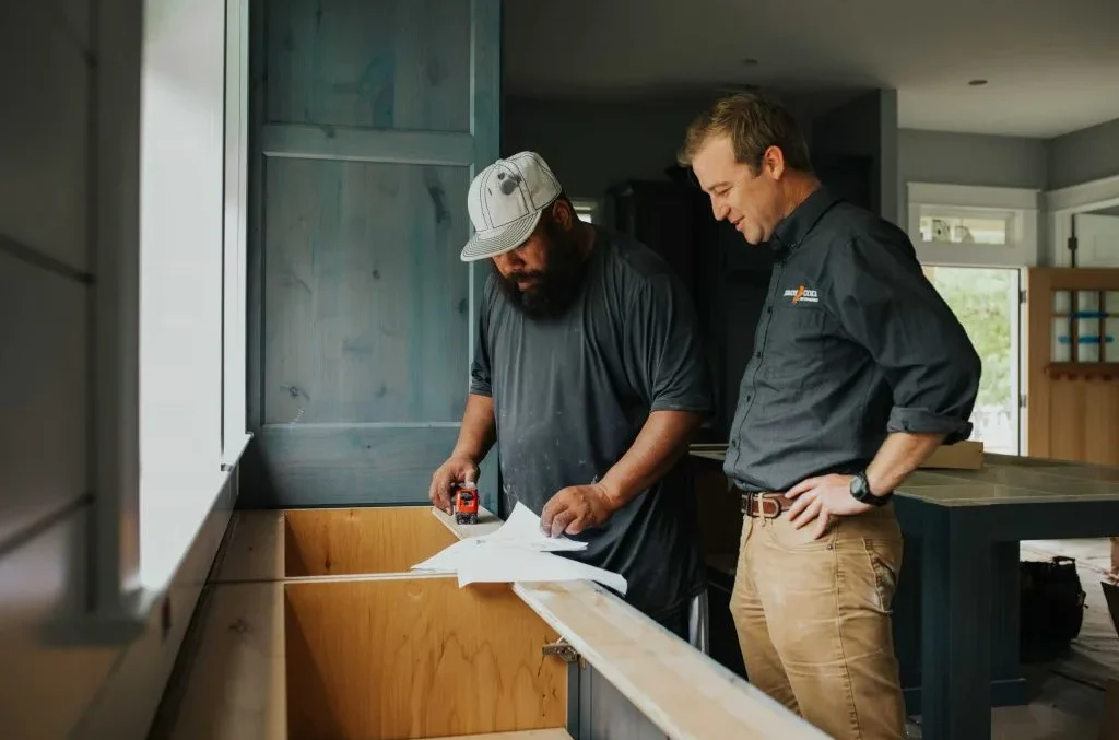 Two pros looking at paper blueprints on wooden kitchen cabinet frame