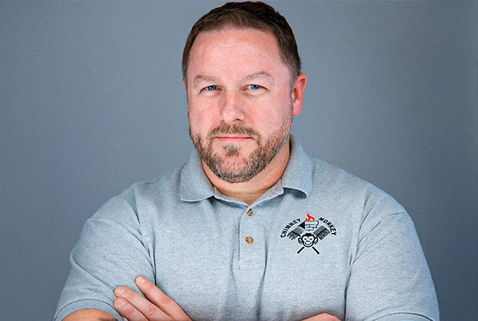 Brett C, owner of Chimney Monkey headshot looks into camera with arms crossed wearing grey collared polo.