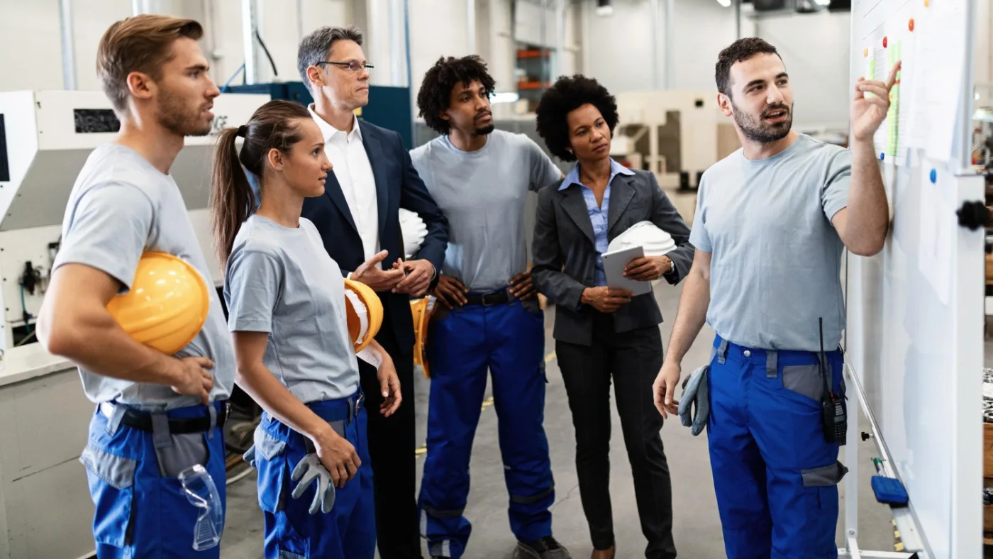 People standing and listening to a person pointing at notes or papers on the board