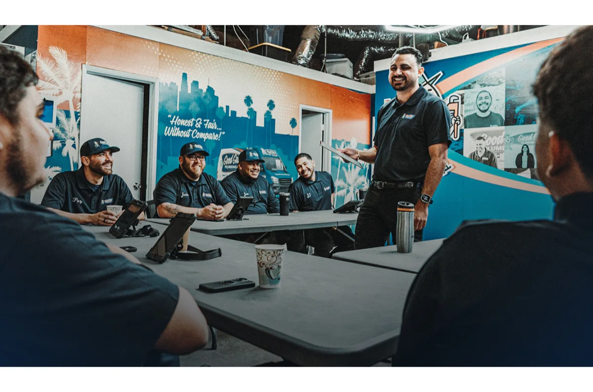 Team leader giving a presentation to service professionals during a meeting, with team members listening and smiling around a conference table.