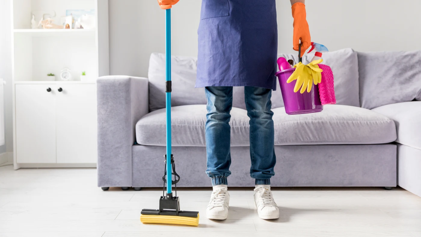 House cleaning professional holding mop and cleaning bucket in a tidy living room.