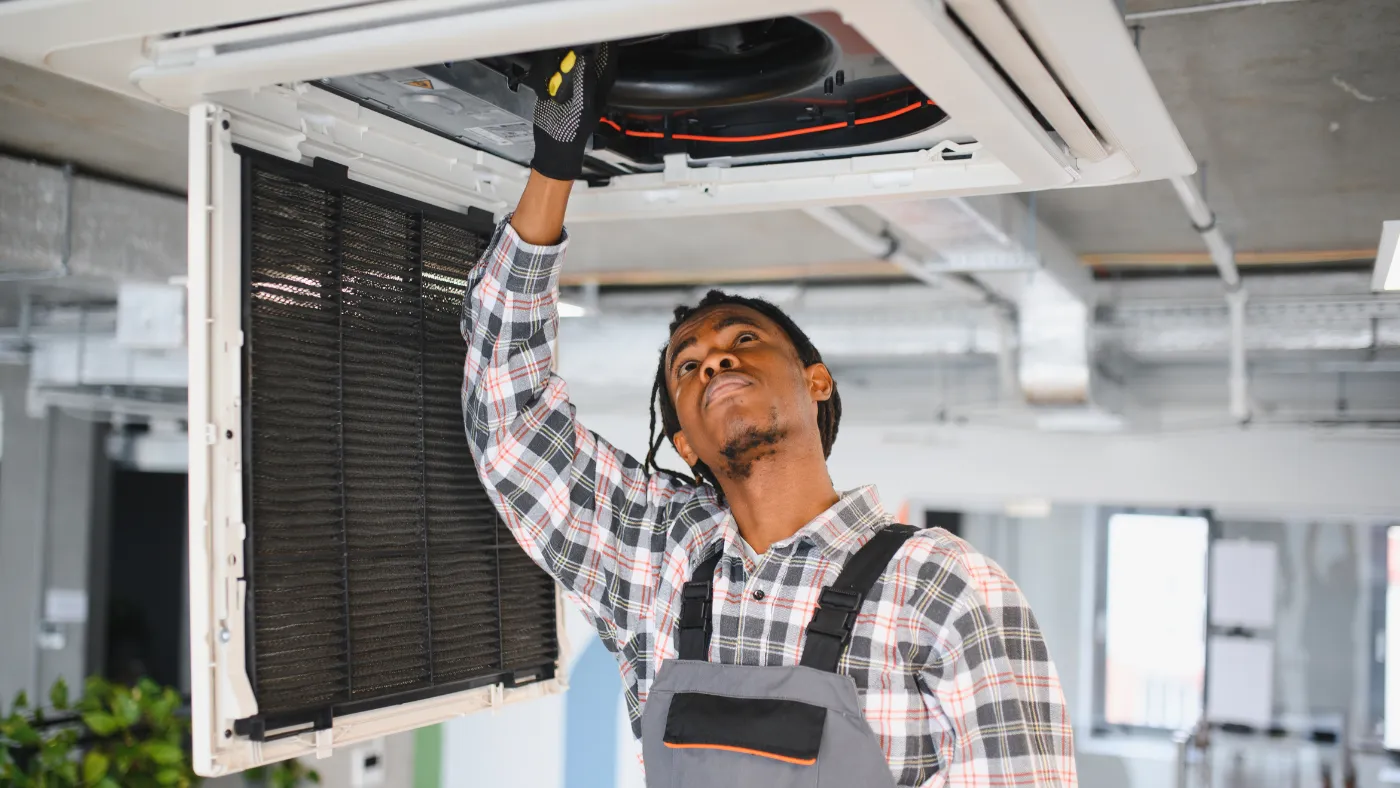 HVAC technician inspecting and repairing a ceiling-mounted air conditioning unit in a commercial building.