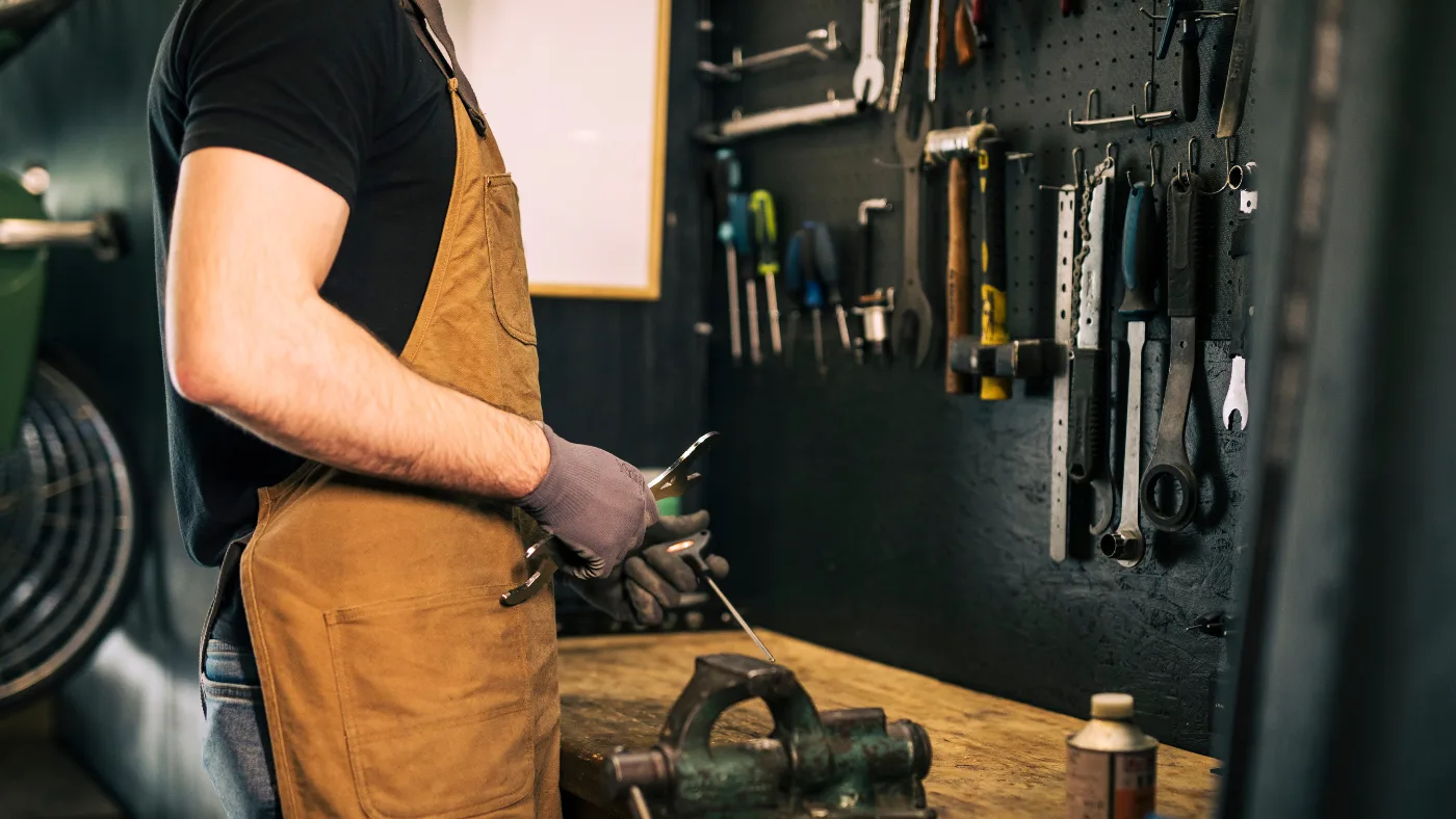 Handyman in workshop using tools at workbench with hanging equipment.