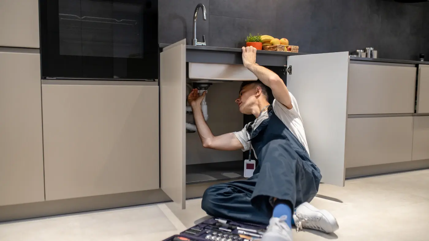 Plumber inspecting pipe under sink in kitchen
