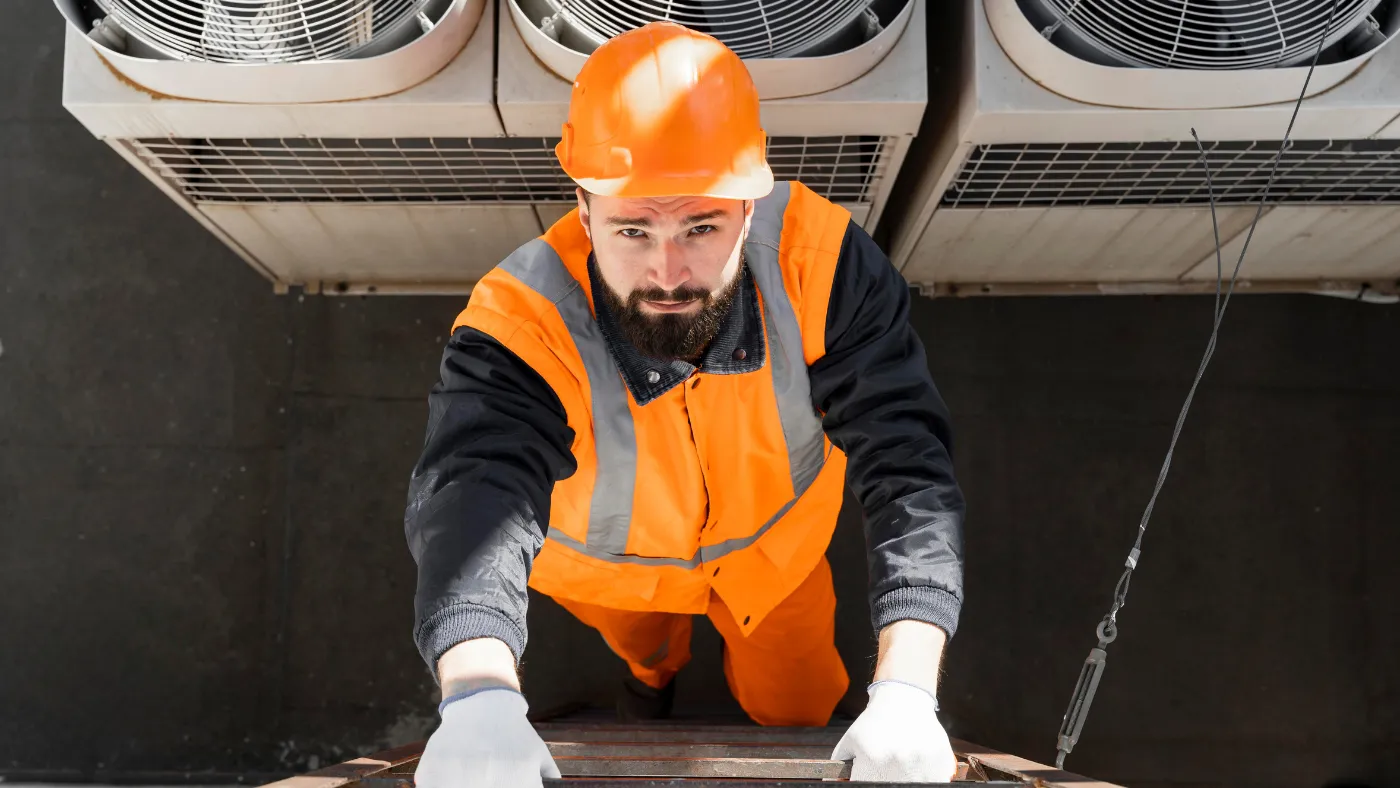 HVAC worker in safety gear climbing a ladder near rooftop air conditioning units